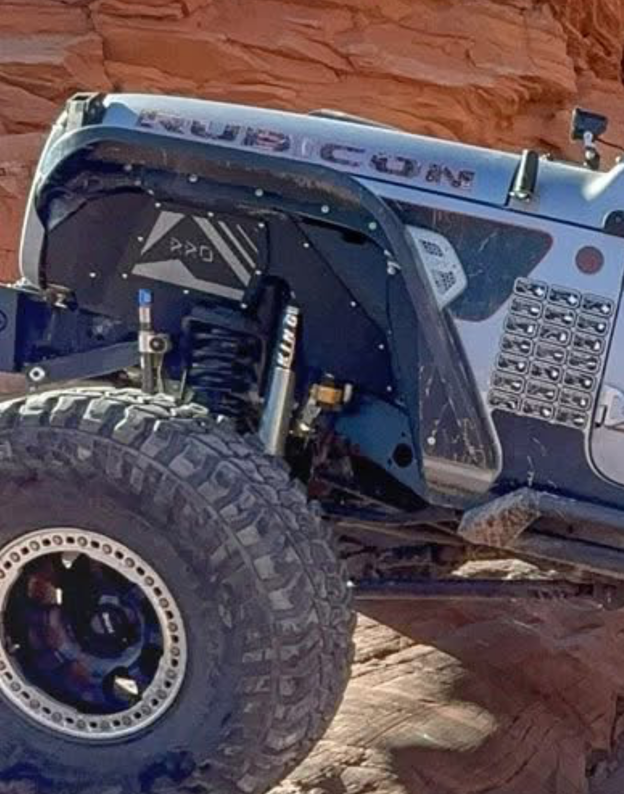 Off-road vehicle climbing a rocky incline with Rock Ready Inner Fenders branding.